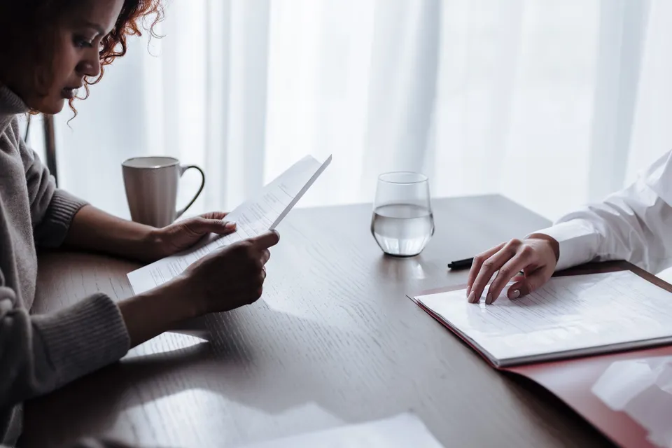 Two women reviewing documents with coffee and water on a table.